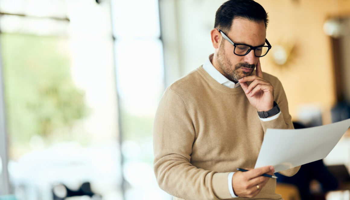 Professional Man Reading Document in Modern Office, Focused and Thoughtful, Glasses On
