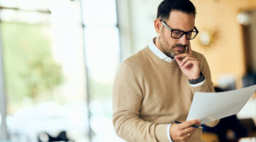Professional Man Reading Document in Modern Office, Focused and Thoughtful, Glasses On