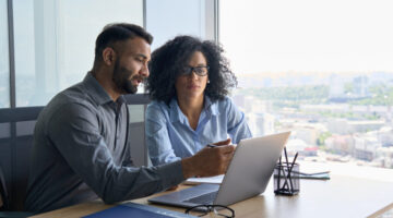 Multiethnic colleagues sitting at desk looking at laptop computer in office.