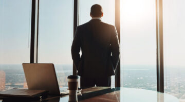 Business, man and back thinking at window in office with city view for legal case ideas and solution. Law firm, thoughtful advocate and professional or contemplating client defense for court trial