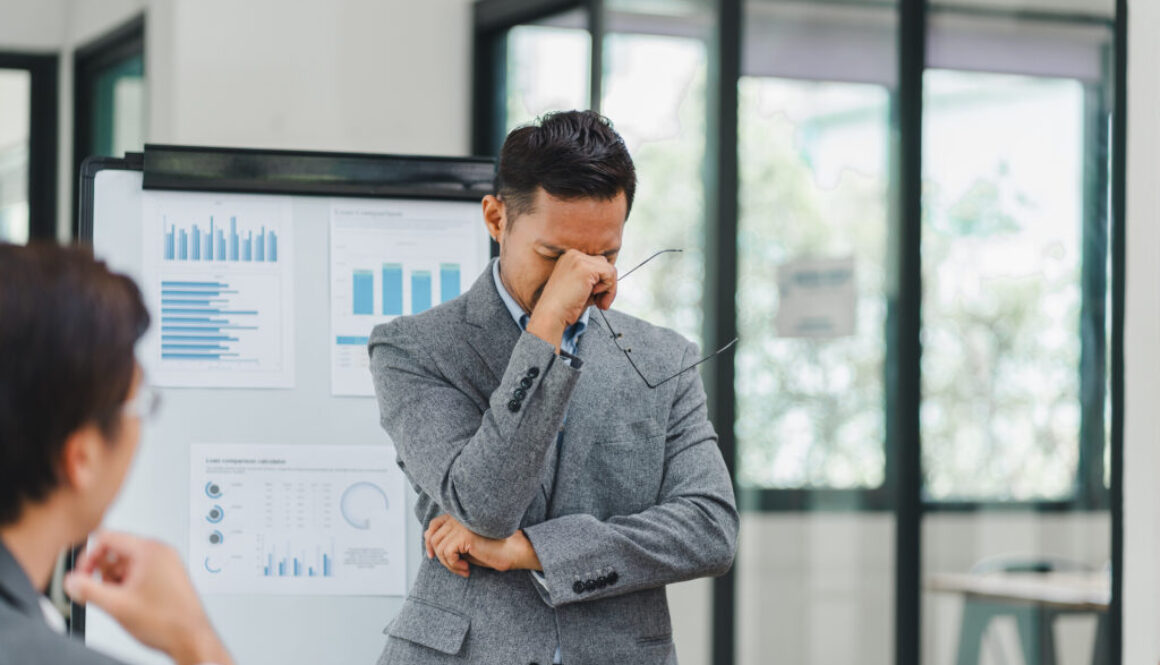 Pensive businessman deep in thought while presenting data charts and graphs during a meeting with colleagues in a modern office.