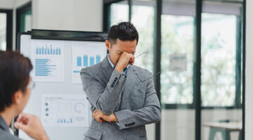 Pensive businessman deep in thought while presenting data charts and graphs during a meeting with colleagues in a modern office.