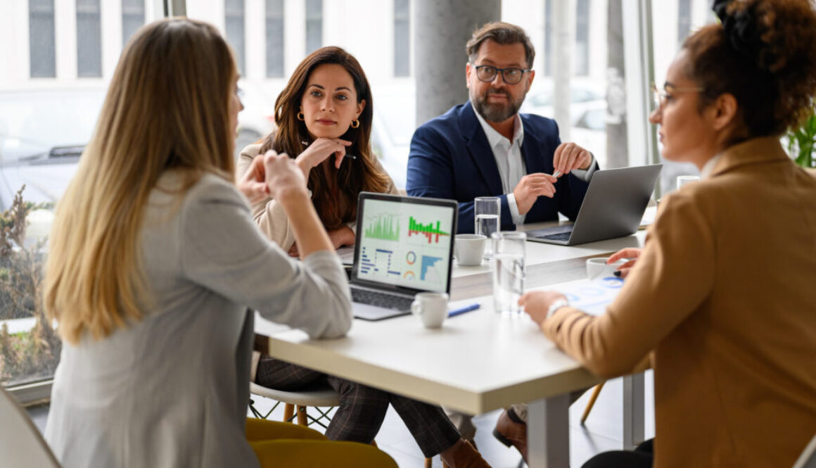 Businesswoman reviewing report on her laptop while discussing business growth with coworkers in meeting