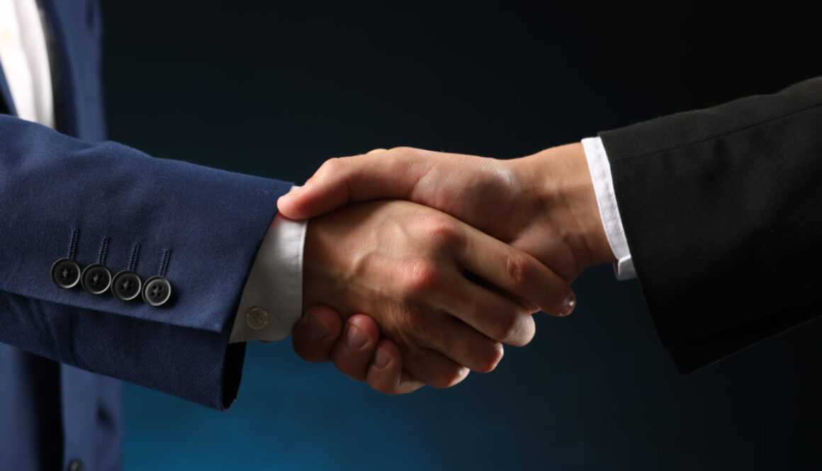 Business partners shaking hands on dark blue background, closeup