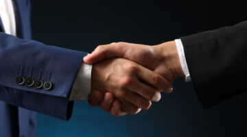 Business partners shaking hands on dark blue background, closeup